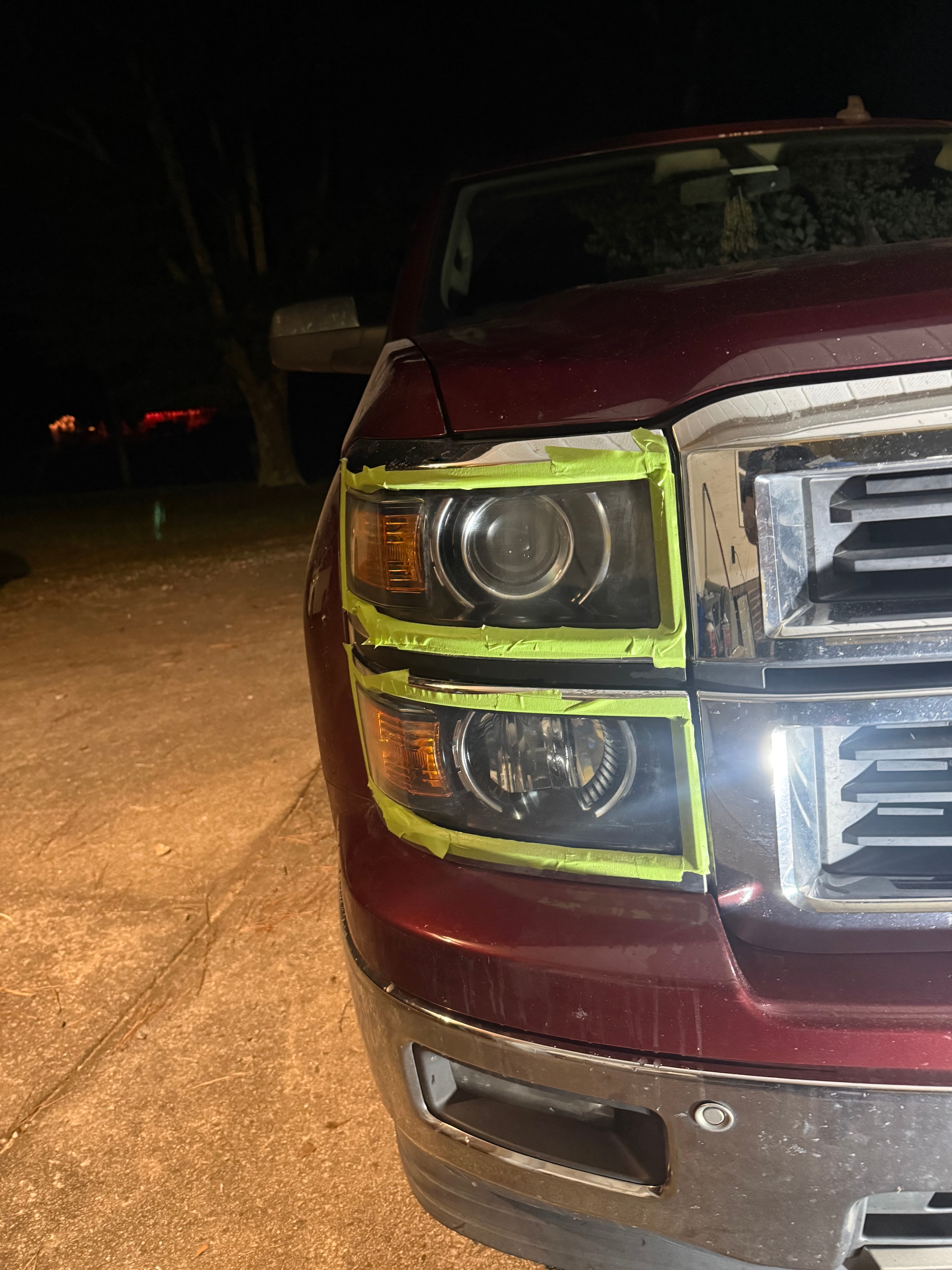 Red vehicle headlights taped with neon green tape mid-restoration